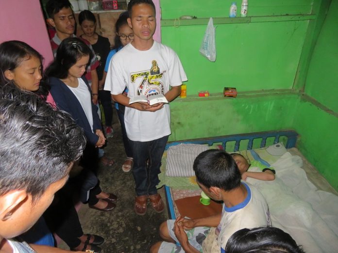 Fr. Gusti SMM memimpin doa bersama Pak Saimun dan di depan Rendy yang terbaring di dipan.