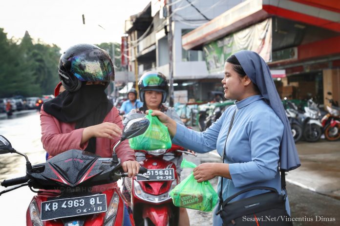 Suster Maria Seba SFIC berbagi takjil kepada pengendara yang melaju di jalanan dekat Gereja Katedral Pontianak, Kalbar, Jumat (8/6/18) petang menjelang waktu berbuka puasa. Kegiatan "Takjil for Care" ini dibesut oleh para ibu anggota WKRI Gereja Katedral Pontianak. (Vincent Dimas/Sesawi.Net)